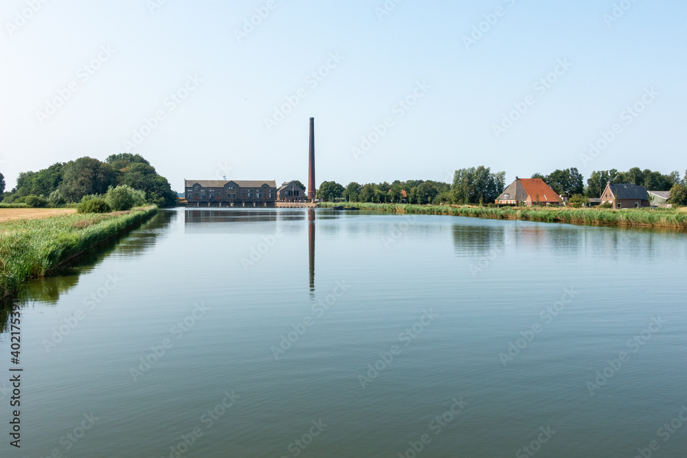 Steam pumping station with long pipe, reflecting in windless canal, Woudagemaal in Lemmer, Friesland, UNESCO World Heritage Steam pumping station with long pipe, reflecting in windless canal, Woudagemaal in Lemmer, Friesland, UNESCO World Heritage