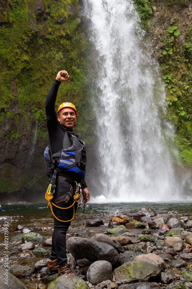 Obraz premium A vertical shot of a Hispanic cheerful rock climber in a helmet hat and safety harness celebrating an achievement