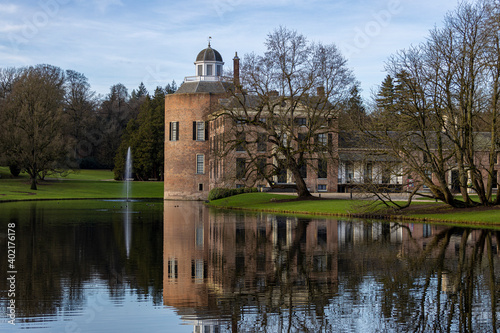 Tower and mansion of Rosendael castle with barren winter trees in front reflecting in the still water of the garden pond in the foreground