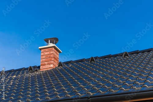 Foto New chimney pipe in red bricks on roof in black shingles