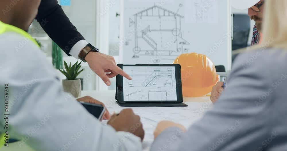 Front view of working process with customers and contractors which revisioning together building project on tablet pc during meeting in boardroom