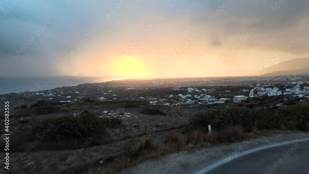 Aerial shot flying over a road and revealing Santorini island on a dramatic sunrise Aerial shot flying over a road and revealing Santorini island on a dramatic sunrise