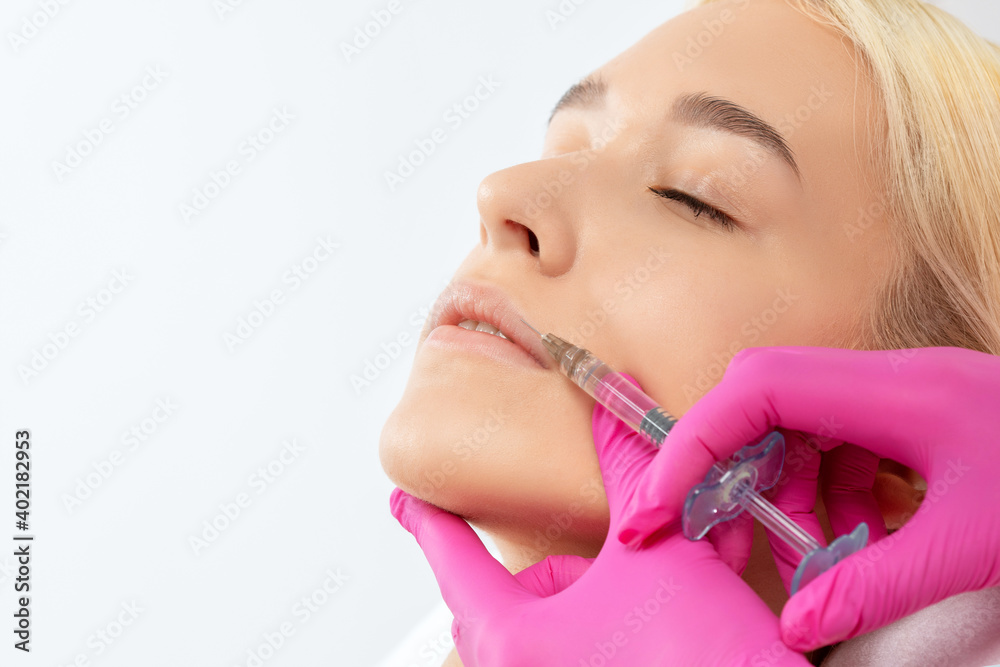 Cosmetologist does injections for lips augmentation and anti wrinkle in the nasolabial folds of a beautiful woman. Women's cosmetology in the beauty salon. Cosmetologist does injections for lips augmentation and anti wrinkle in the nasolabial folds of a beautiful woman. Women's cosmetology in the beauty salon.