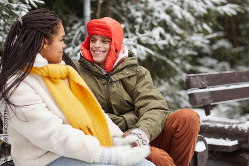 Happy young man smiling to woman during their conversation on the bench in winter park