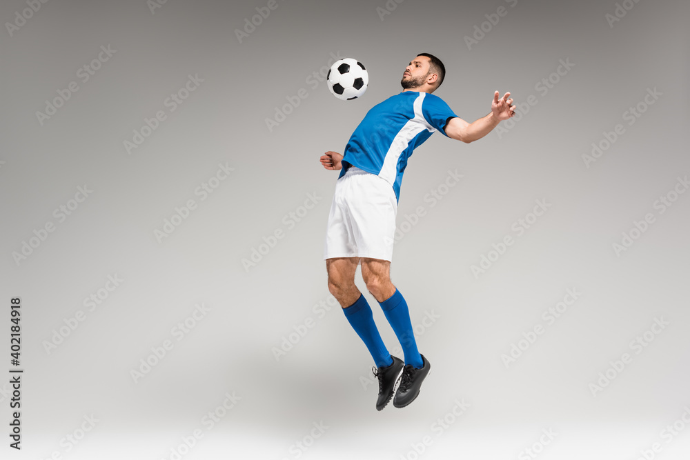 Fototapeta premium Sportsman training with football while jumping on grey background