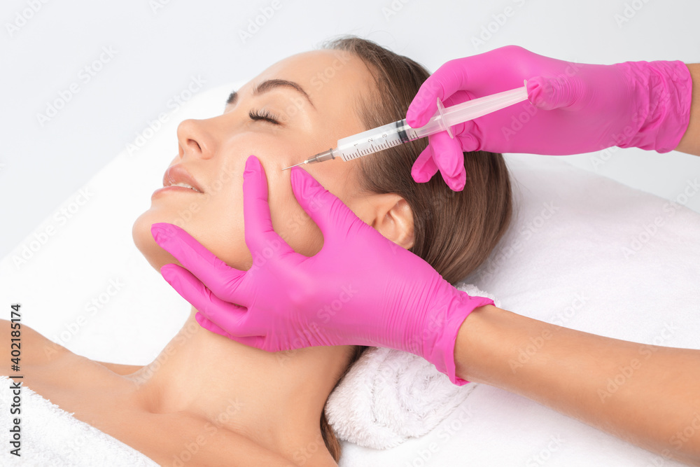 Fototapeta premium Cosmetologist makes lipolytic injections to burn fat on the chin, cheeks and neck of a woman against double chin. Female aesthetic cosmetology in a beauty salon.Cosmetology concept.