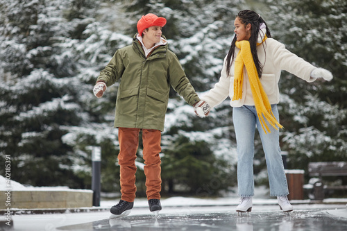 Two friends in warm clothing enjoying the leisure time outdoors skating on skating rink