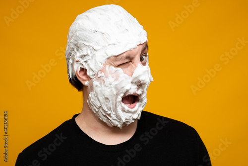 The Caucasian man winks, shaving foam covering his entire face. On a yellow background.