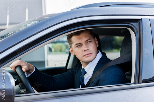 Businessman looking at window while driving auto on blurred foreground.