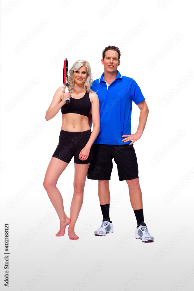 Portrait of a fit, young, white coach & barefoot female athlete with curly long blond hair posing together holding a tennis racquet in a studio with white background wearing black shorts & sports bra. Portrait of a fit, young, white coach & barefoot female athlete with curly long blond hair posing together holding a tennis racquet in a studio with white background wearing black shorts & sports bra.
