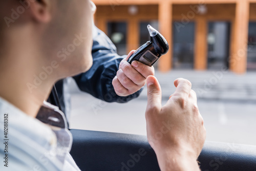 cropped view of policeman giving breathalyzer to driver in car, blurred foreground.