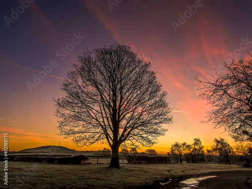 A view across the frost-covered fields at Wroxeter, UK through the early morning mist towards the Wrekin hill with a fiery sky just before sunrise photo
