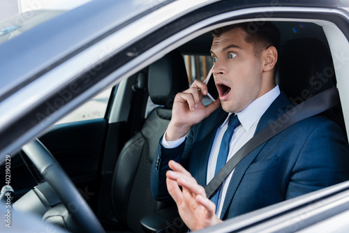 Scared businessman talking on smartphone on driver seat of car.