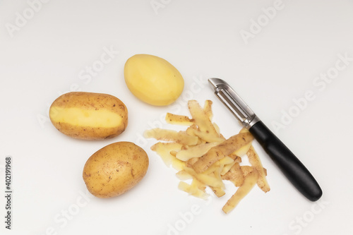 Raw peeled potatoes with a potato peeler on a white table, potato peel.