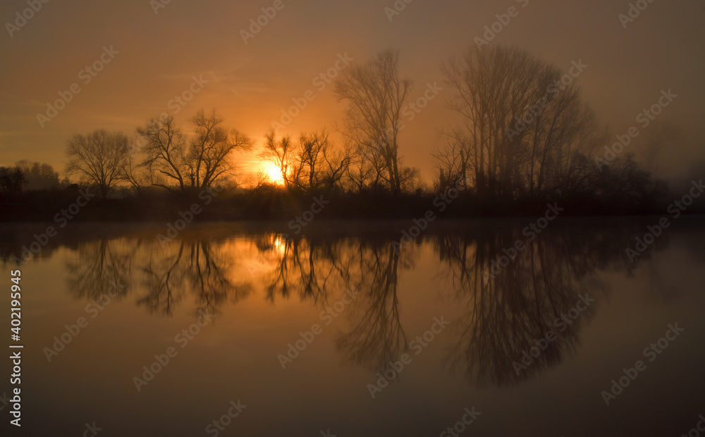 Spiegelung eines idyllischen Sonnenaufgangs an einem nebligen Morgen