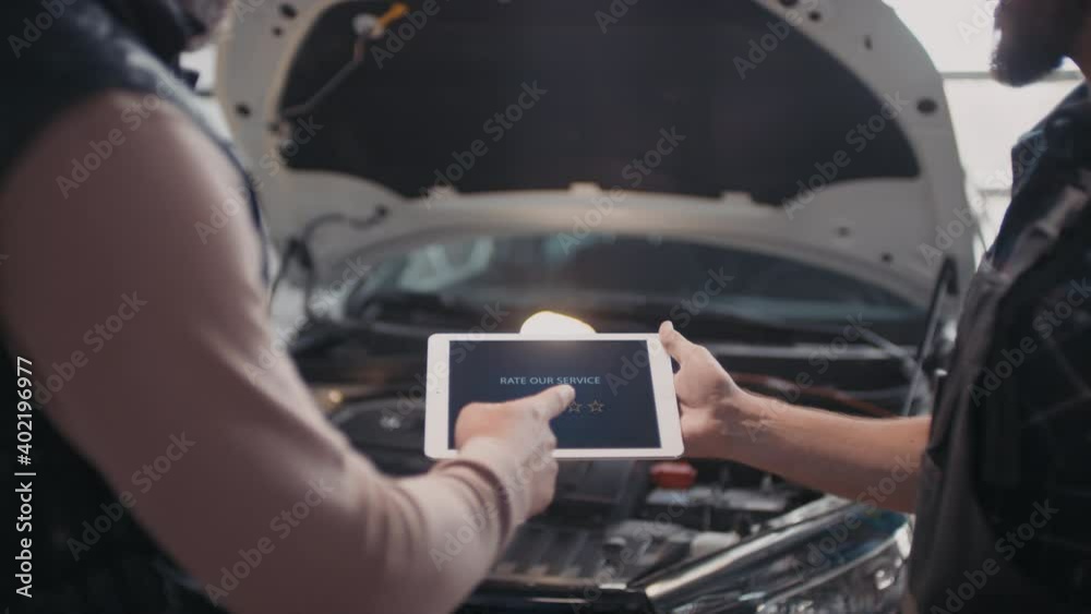 Mid-section shot of unrecognizable male auto mechanic explaining repairs done on clients car and suggesting him to rate their service on tablet Mid-section shot of unrecognizable male auto mechanic explaining repairs done on clients car and suggesting him to rate their service on tablet