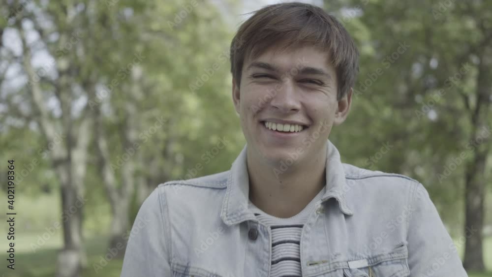 Close-up portrait of happy young Caucasian man looking at camera and laughing out loud. Headshot of handsome brunette guy standing in sunny summer park. Happiness and lifestyle concept. Close-up portrait of happy young Caucasian man looking at camera and laughing out loud. Headshot of handsome brunette guy standing in sunny summer park. Happiness and lifestyle concept.