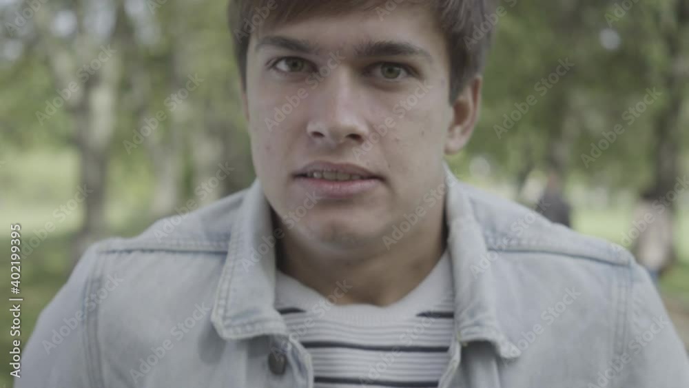 Close-up face of furious young man screaming outdoors. Headshot portrait of angry brunette Caucasian guy shouting and looking at camera standing in summer park. Nervous breakdown. Close-up face of furious young man screaming outdoors. Headshot portrait of angry brunette Caucasian guy shouting and looking at camera standing in summer park. Nervous breakdown.