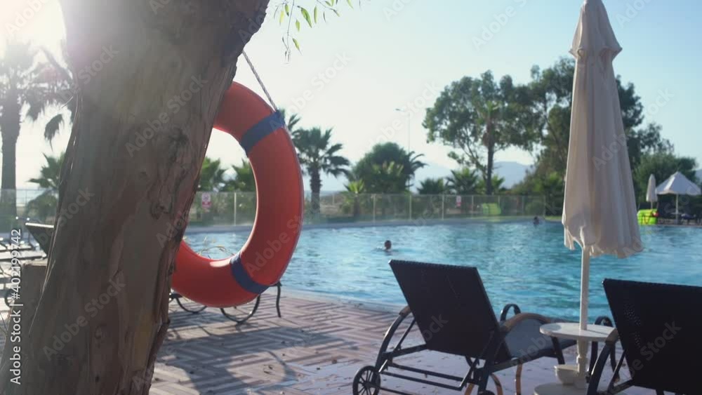 Bright colour lifebuoy hangs on tree near swimming pool of resort hotel. Life safety concept.
