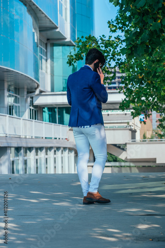 Back view of a stylish young businessman talking on his phone while standing outside his office