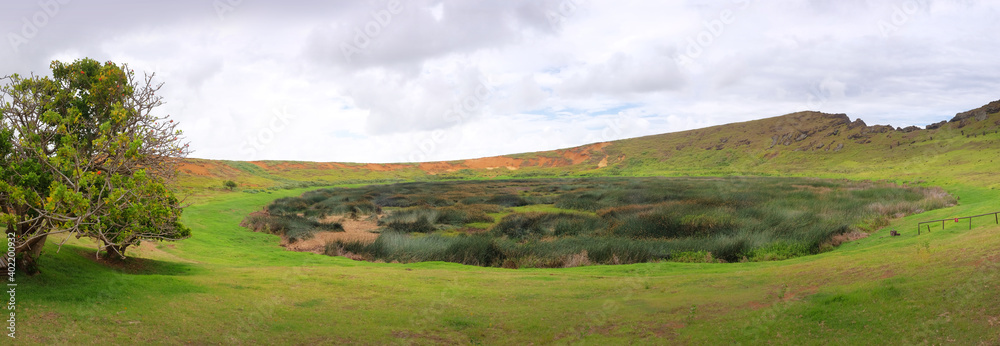 Panoramic view inside the crater of Rano Raraku volcano on Easter Island, against a blue sky, covered by white clouds.