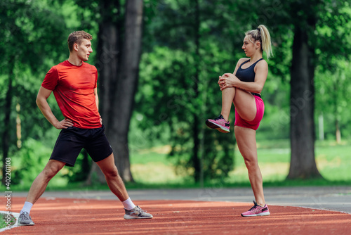 Young couple stretching before starting their morning jogging routine on a tartan track at the park.