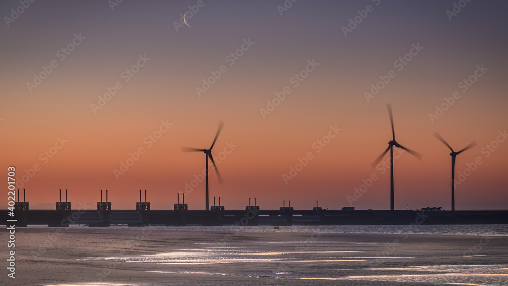 The sky turns orange during sunrise above the Eastern Scheldt storm surge barrier and some windmills in the Netherlands