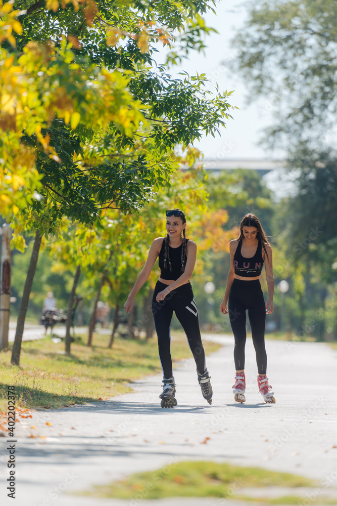 Fototapeta premium Full-length picture of sexy sportswomen rollerskating in the park