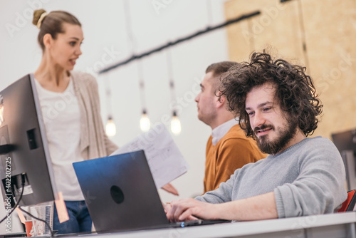 Coworkers, employees working and discussing a project they are preparing while typing on a laptop and looking at pc, computer.