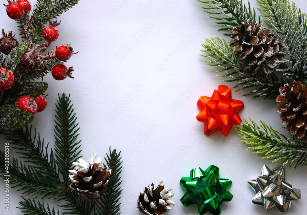 Christmas greeting card mockup with snow covered pine cone, spruce branches, red holly berries and silver, green, orange festive gift bows on white background. Top view. Flat lay. Christmas greeting card mockup with snow covered pine cone, spruce branches, red holly berries and silver, green, orange festive gift bows on white background. Top view. Flat lay.