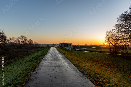 Bike path over a dyke with a water pumping station facility in the distance regulating water levels in Dutch river landscape and its floodplains near Zutphen at early morning sunrise