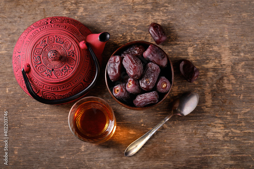 Cup with dates, mug of tea and teapot on dark background, top view