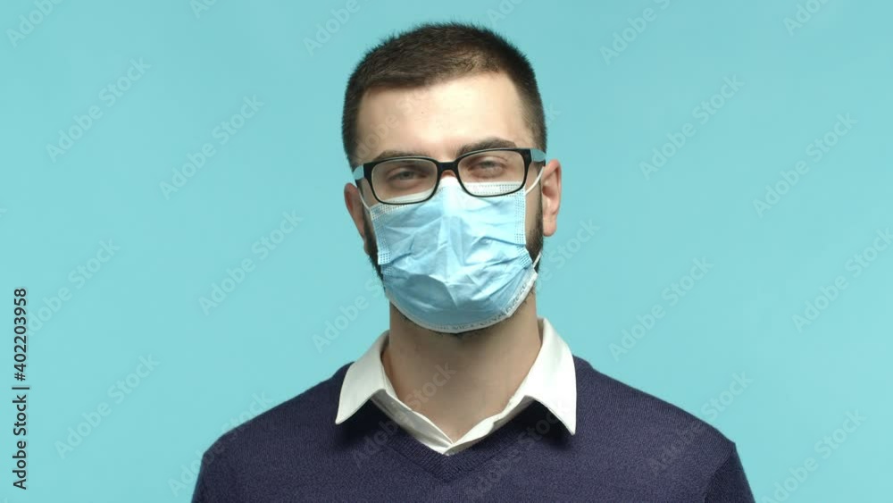 Covid-19, quarantine and pandemic concept. Slow motion of adult caucasian man in glasses and medical mask nodding, understand and agree, standing over blue background Covid-19, quarantine and pandemic concept. Slow motion of adult caucasian man in glasses and medical mask nodding, understand and agree, standing over blue background
