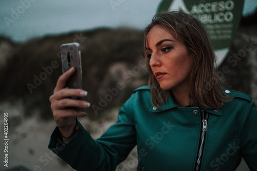  Chica rubia feliz en una playa de otoño invierno al sur de españa haciendo selfie vestida a la moda llamativa casual photo