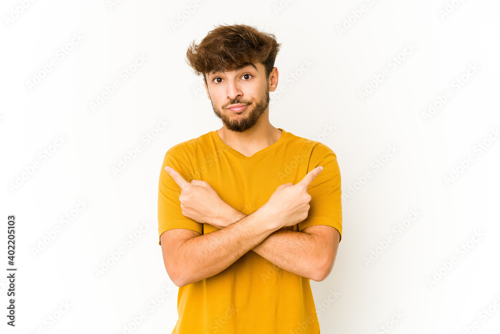 Young arab man on white background points sideways, is trying to choose between two options.