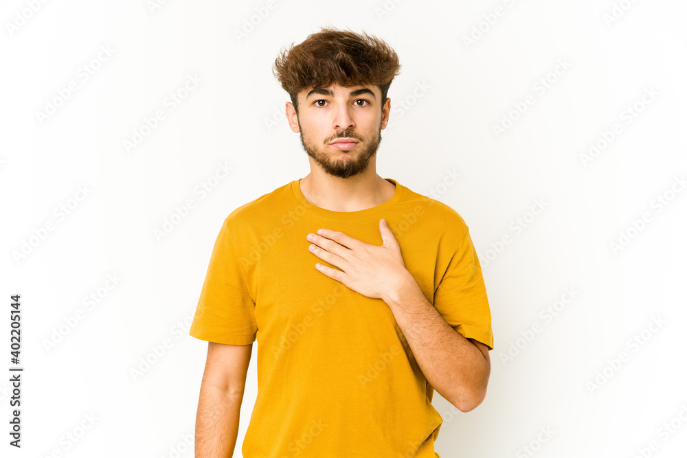 Young arab man on white background taking an oath, putting hand on chest.