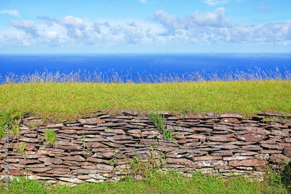 Ruins of the ceremonial village of Orongo, in the archaeological site on the Rano Kau volcano, on Easter Island - Rapa Nui, surrounded by green vegetation, against a blue clear sky.