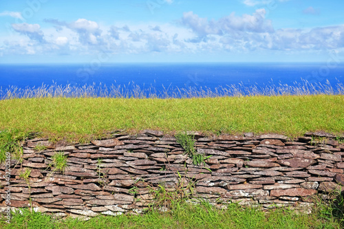 Ruins of the ceremonial village of Orongo, in the archaeological site on the Rano Kau volcano, on Easter Island - Rapa Nui, surrounded by green vegetation, against a blue clear sky.