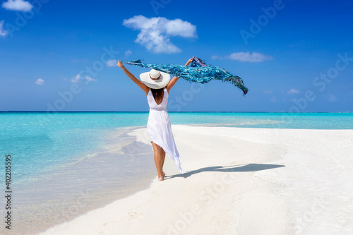 Fotografie A elegant tourist woman in white summer dress walks on a tropical beach with a w