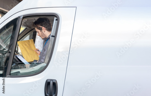 Carrier with uniform in driver's seat looking at the packages to deliver the orders.