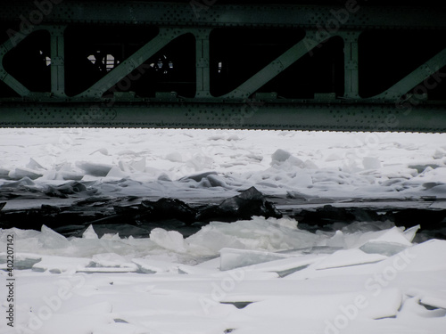 Broken ice under white snow on the river in winter under the bridge.