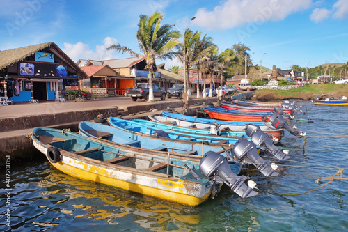 Colorful boats in the port of Hanga Roa, near Plaza Hotu Matua, surrounded by palm trees, against a blue sky. photo