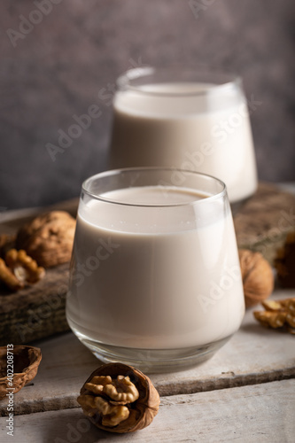 Organic walnut nuts and glass of walnut milk on wooden background.