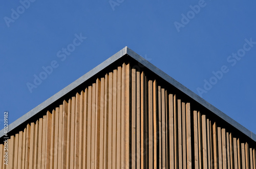 Detail of the roof of a modern building with vertical larch slats cladding against bright blue sky. Perspective view from below.