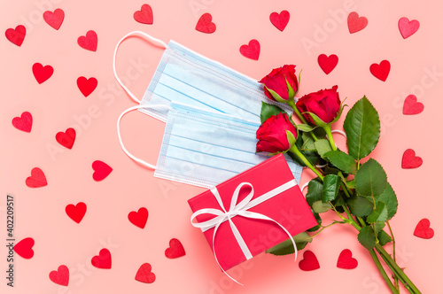 Fototapeta Naklejka Na Ścianę i Meble -  Red roses, gift box and face masks on pink background with many wooden hearts. Mothers, womens or Valentines day celebration during coronavirus pandemic. New normal, dating, love and Covid-19 concept