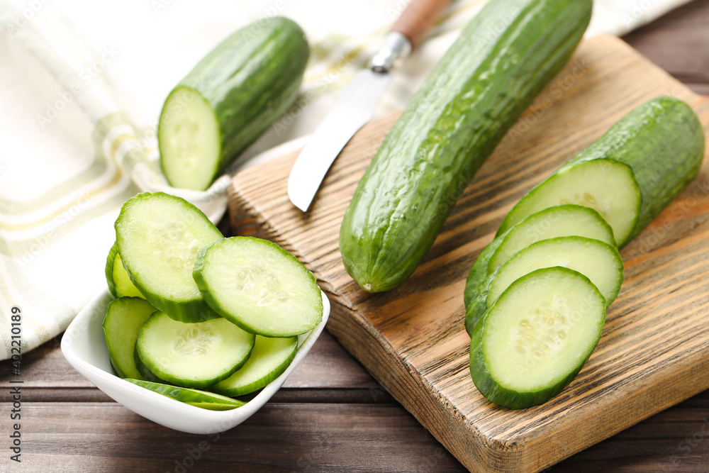 Fresh cucumbers, slices on cutting board and in bowl on brown wooden background Fresh cucumbers, slices on cutting board and in bowl on brown wooden background