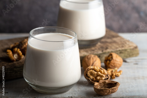 Organic walnut nuts and glass of walnut milk on wooden background.