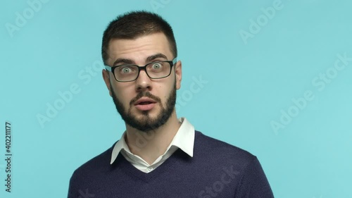 Slow motion of impressed male office worker in glasses stare at camera, raising eyebrows surprised and saying wow, looking amazed, standing over blue background