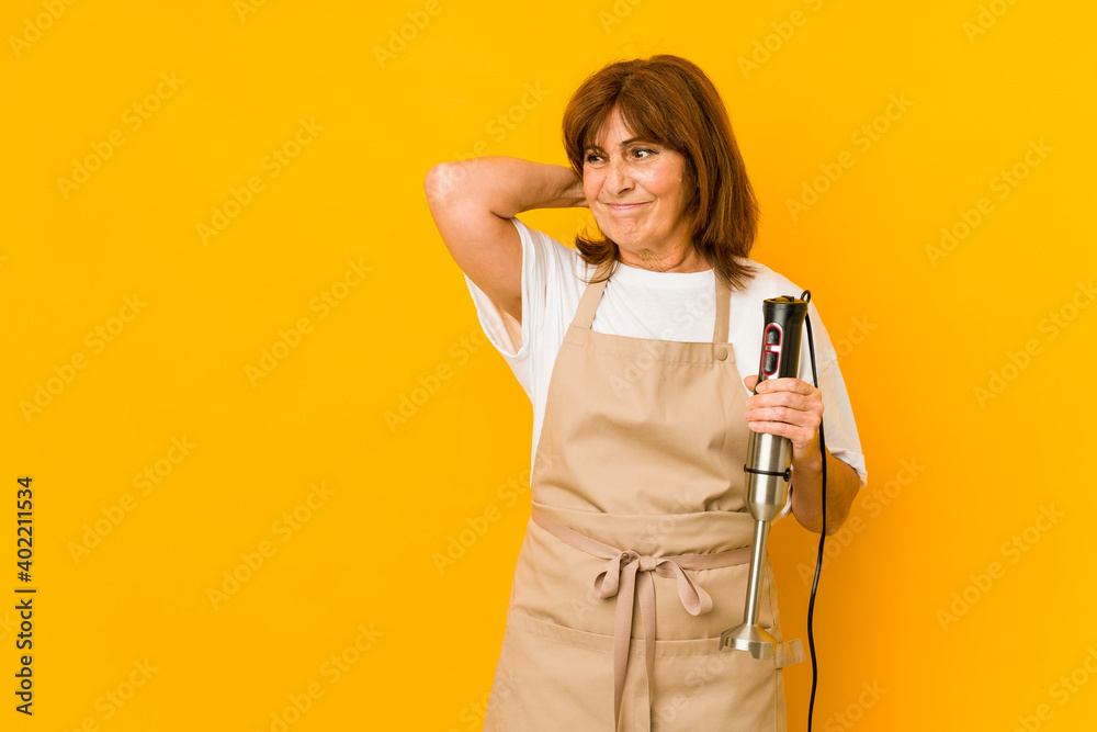 Middle age caucasian cook woman holding a mixer isolated touching back of head, thinking and making a choice.