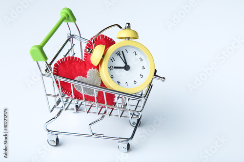 Alarm clock with red fabric heart and shopping cart on blue background
